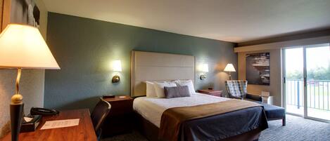 Habitación de hotel con una cama grande, un escritorio con lámpara, una silla y vistas al exterior a través de una puerta corredera.