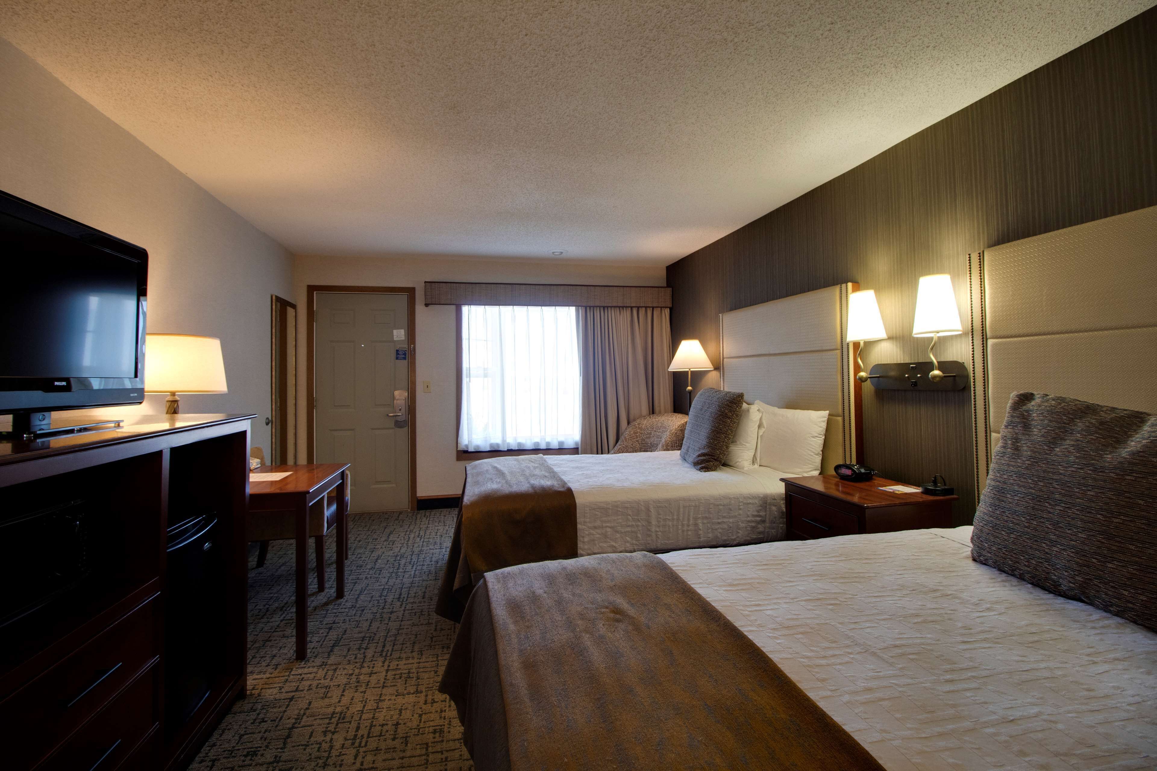 A hotel room with two beds, a television, a desk, and a lamp.