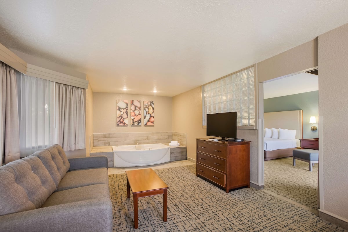 Ein Hotelzimmer mit Sofa, Holztisch, Badewanne, Fernseher, Kommode und Bett.