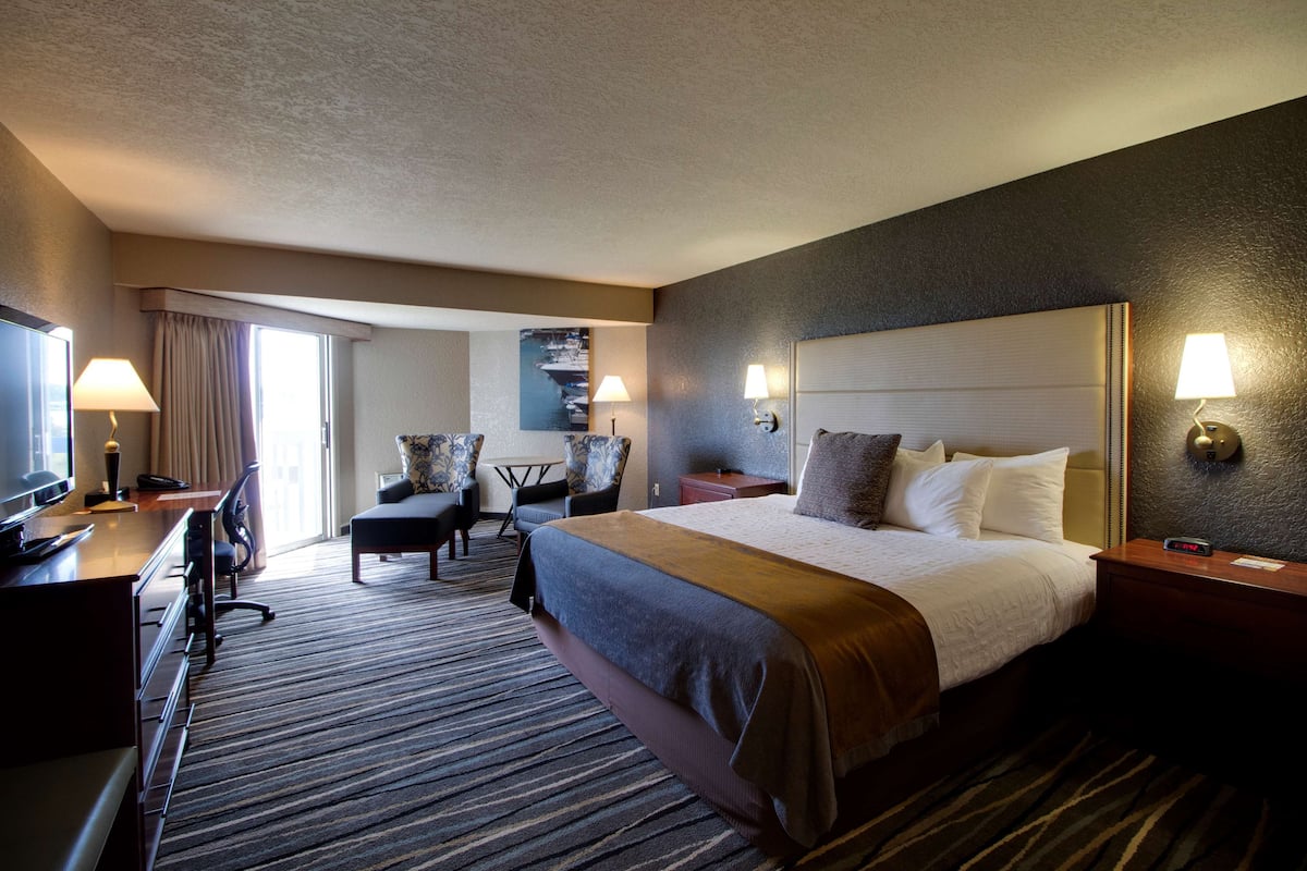 Ein Hotelzimmer mit einem großen Bett, einem Schreibtisch mit Computer, einem Sessel, einer Lampe und einem Fernseher.