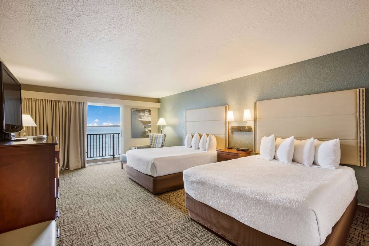 Ein Hotelzimmer mit zwei Betten, einem Schreibtisch, einem Sessel, einem Fernseher und einem Balkon mit Blick.