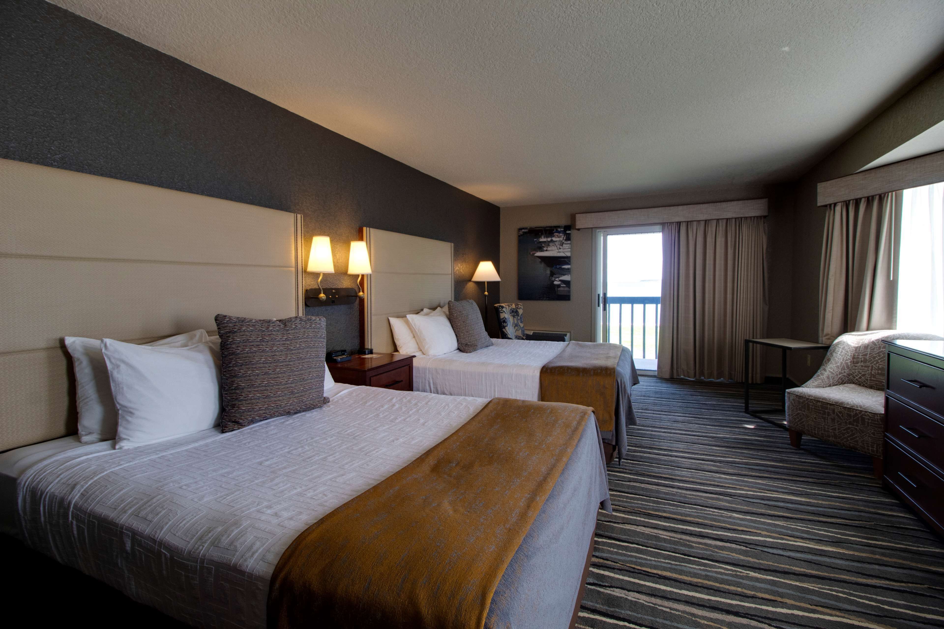 A hotel room with two beds, a desk, a chair, and a large window with curtains.