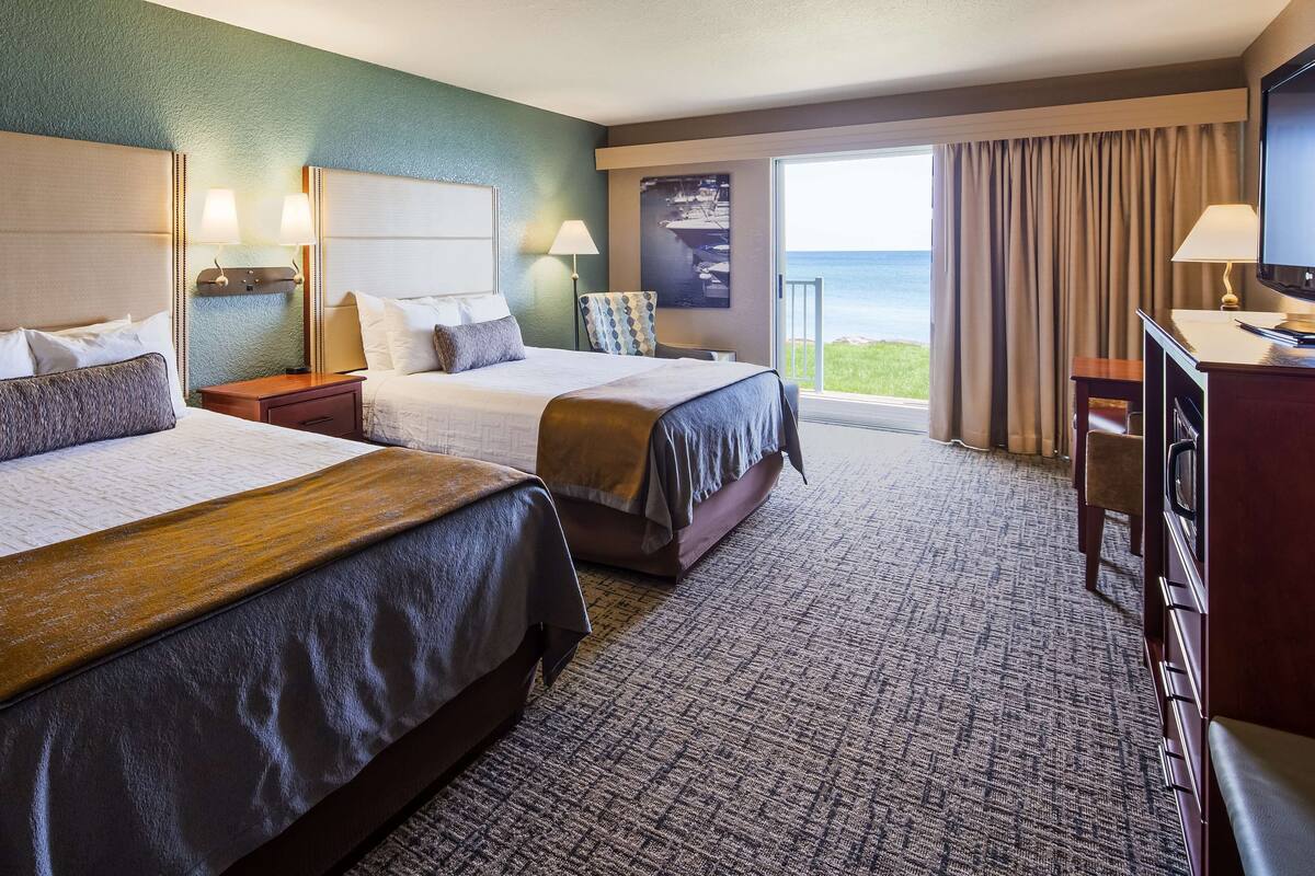 Ein Hotelzimmer mit zwei Betten, einem Schreibtisch, einem Sessel und Meerblick.