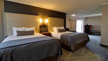 A hotel room with two beds, a nightstand, a desk, and a chair.