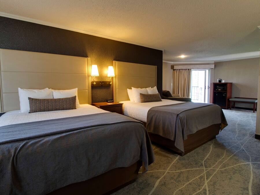A hotel room with two beds, a nightstand, a desk, and a chair.