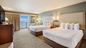 Habitación de hotel con dos camas, un escritorio, una silla y vista al mar.