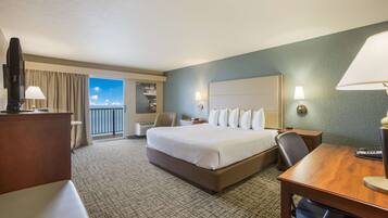 A hotel room with a large bed, a desk, a chair, a TV, and a view of the sky through the window.