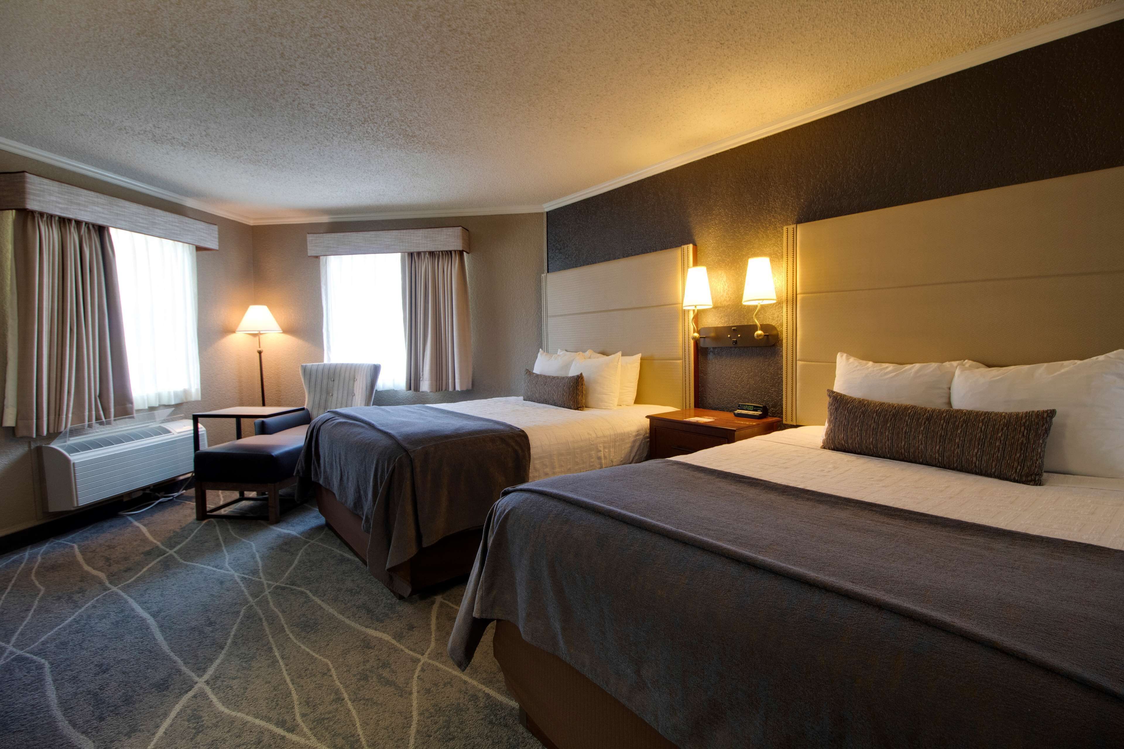 A hotel room with two beds, a chair, a desk, and a lamp.