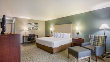 A hotel room with a large bed, a desk, a chair, a TV, and a lamp.