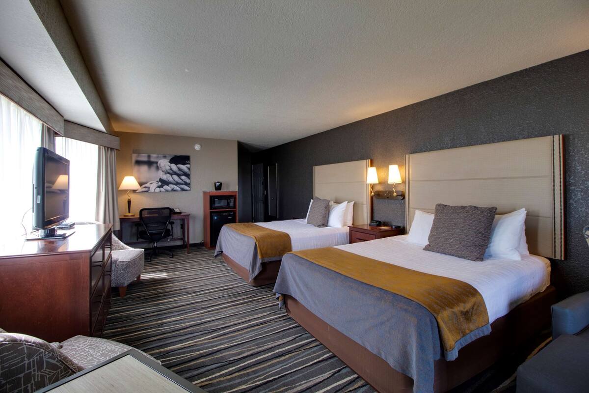 Ein Hotelzimmer mit zwei Betten, einem Schreibtisch mit Computer, einem Fernseher und einer Sitzecke.