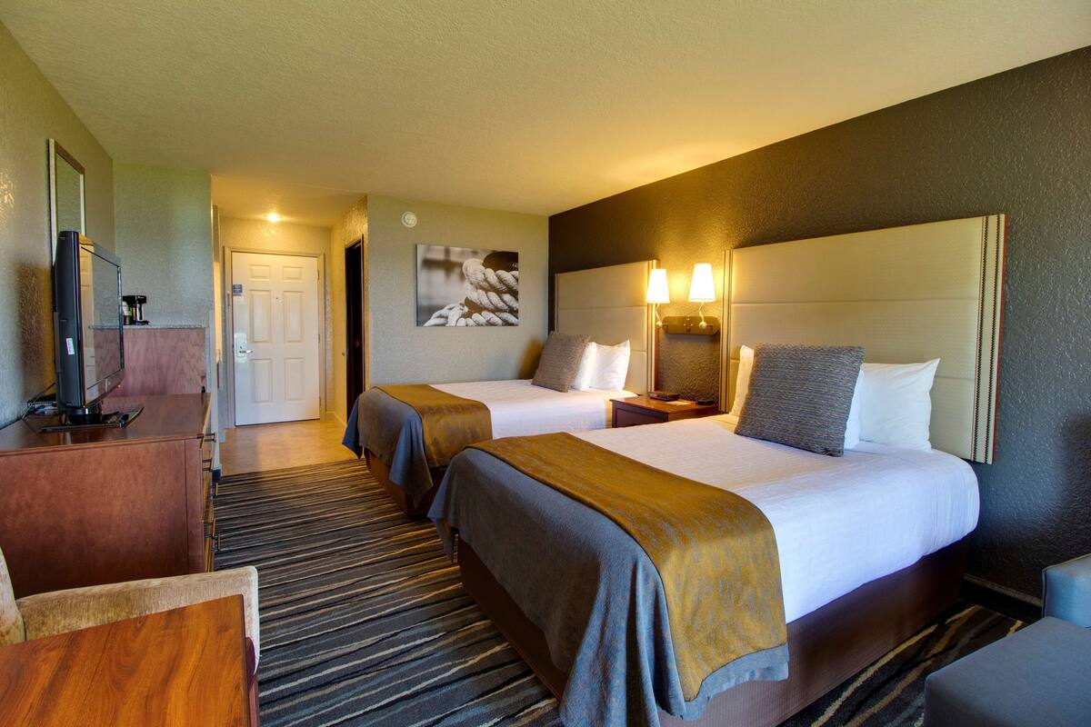 Ein Hotelzimmer mit zwei Betten, einem Fernseher, einem Schreibtisch und einem Badezimmer.