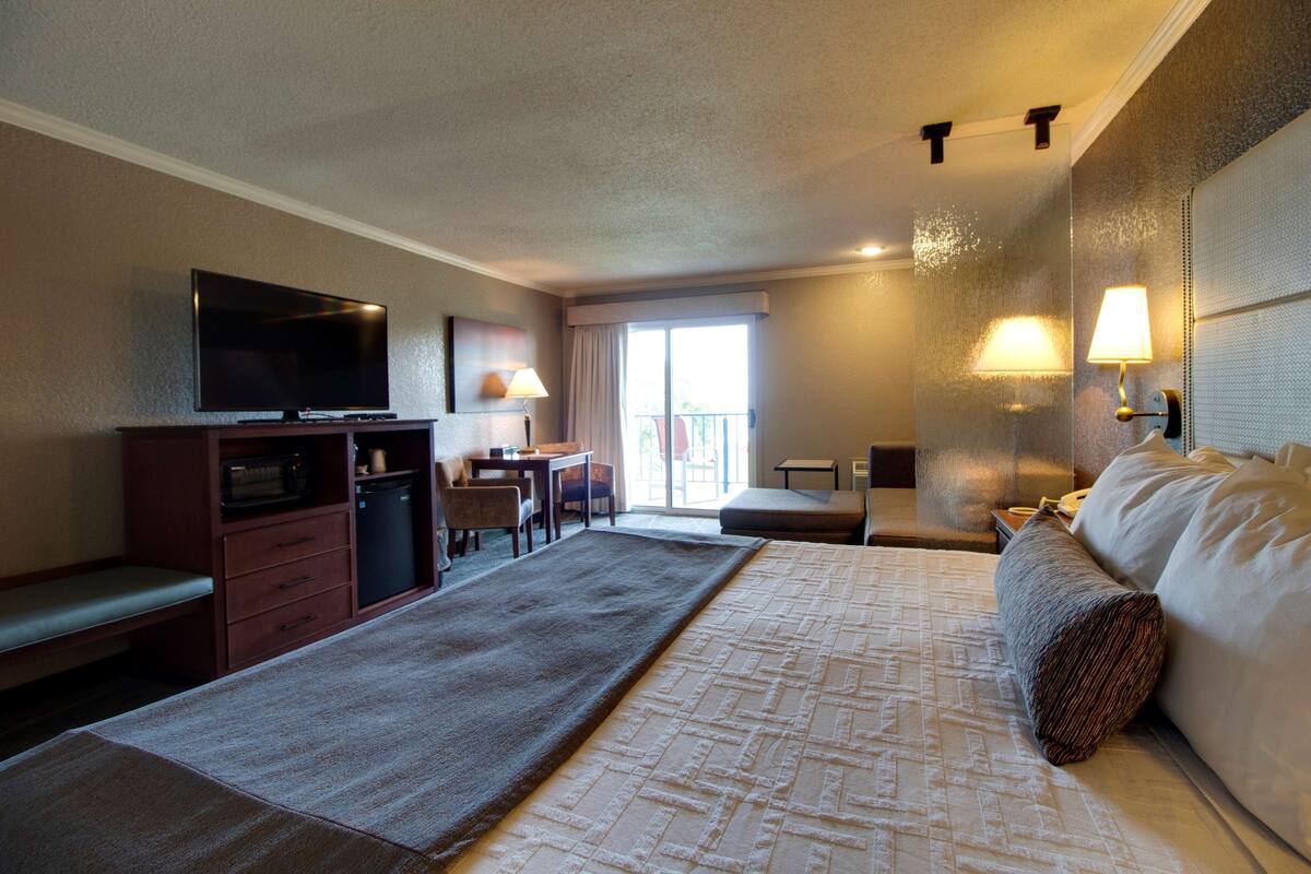 Ein Hotelzimmer mit einem großen Bett, einem Fernseher, einem Schreibtisch und einem Sessel.