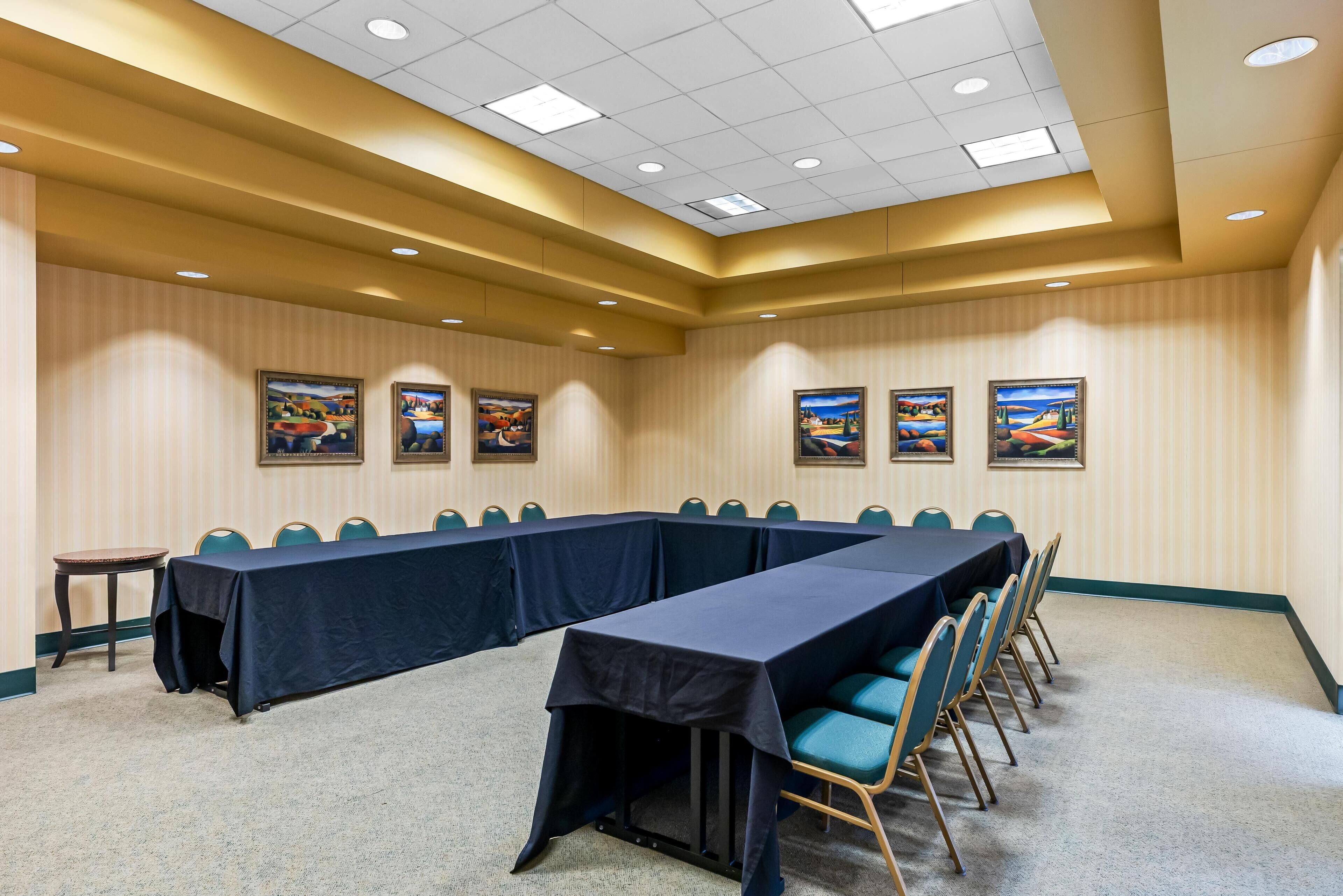 Une salle de conférence avec une longue table, des chaises et des tableaux encadrés accrochés aux murs.
