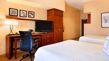 A hotel room with a bed, a desk with a television, a chair, and a cabinet.