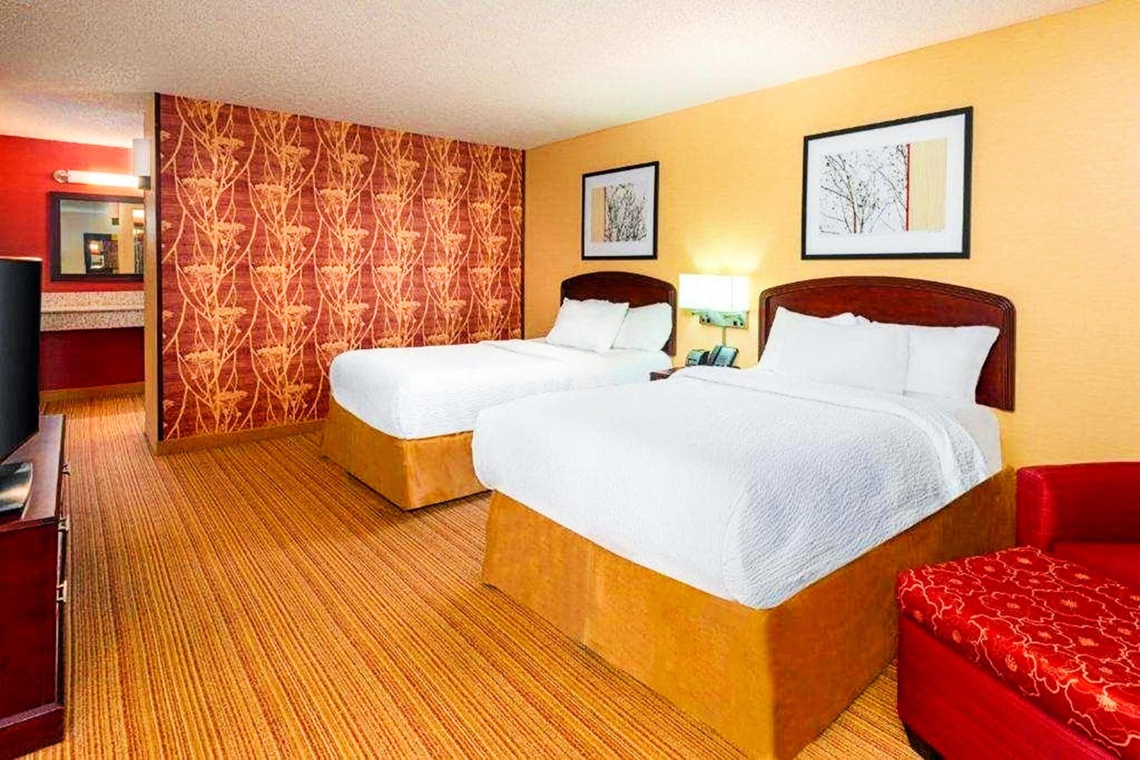 A hotel room with two beds, a red sofa, a television, and artwork on the walls.