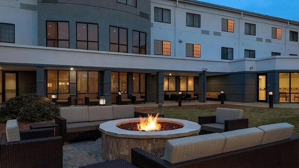 A courtyard with outdoor seating, a fire pit, and a building with large windows.