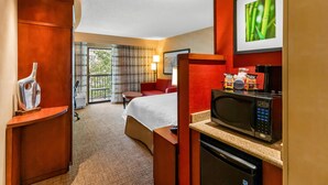 A hotel room with a bed, a desk with a microwave, a red sofa, and a large window with curtains.