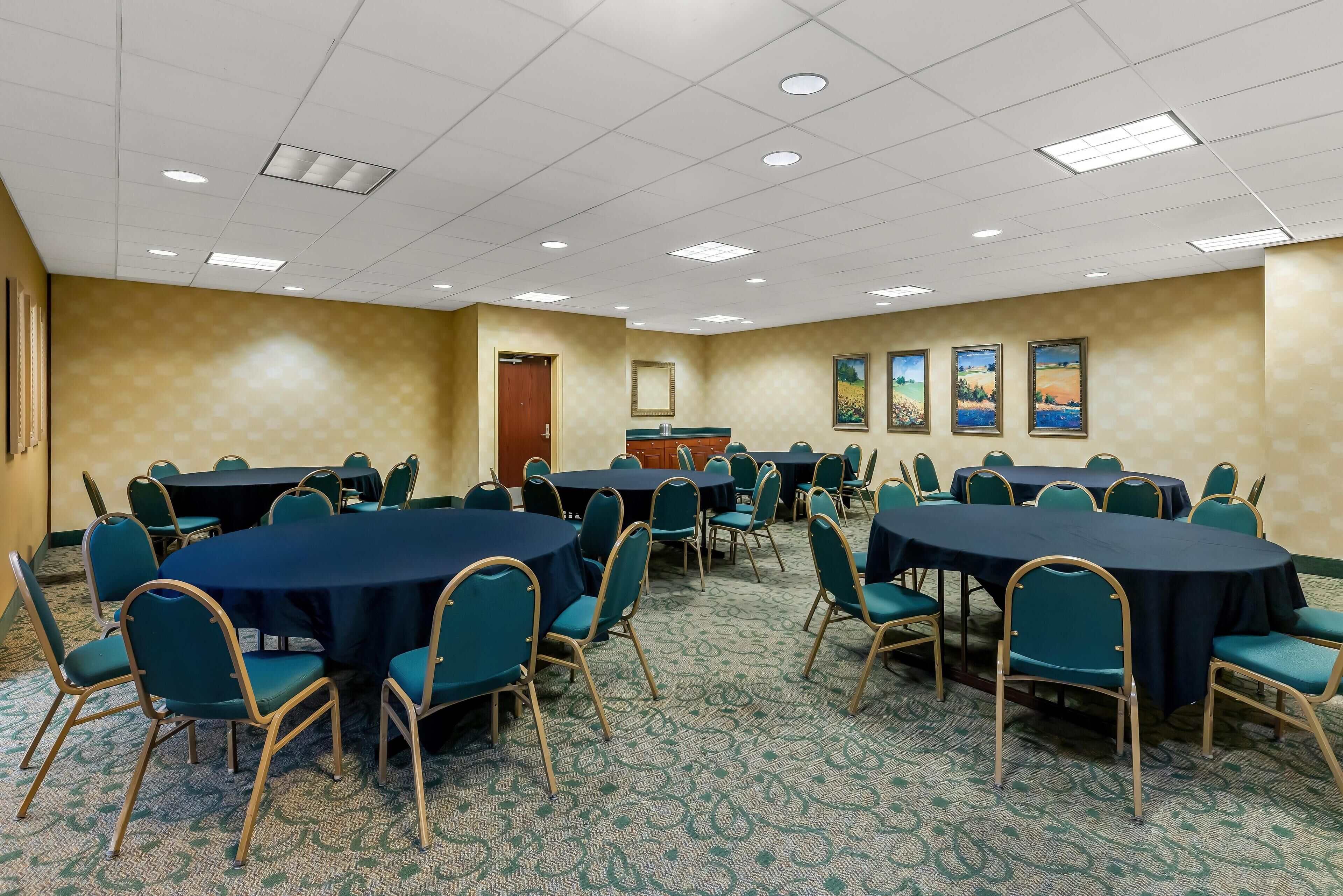 A conference room with round tables and chairs, a podium, and framed pictures on the wall.