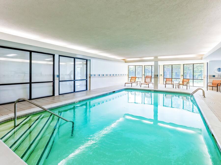 Une piscine intérieure à l’eau claire, dotée d’un sol carrelé et d’un espace aménagé au bord du bassin avec des chaises et un parasol.