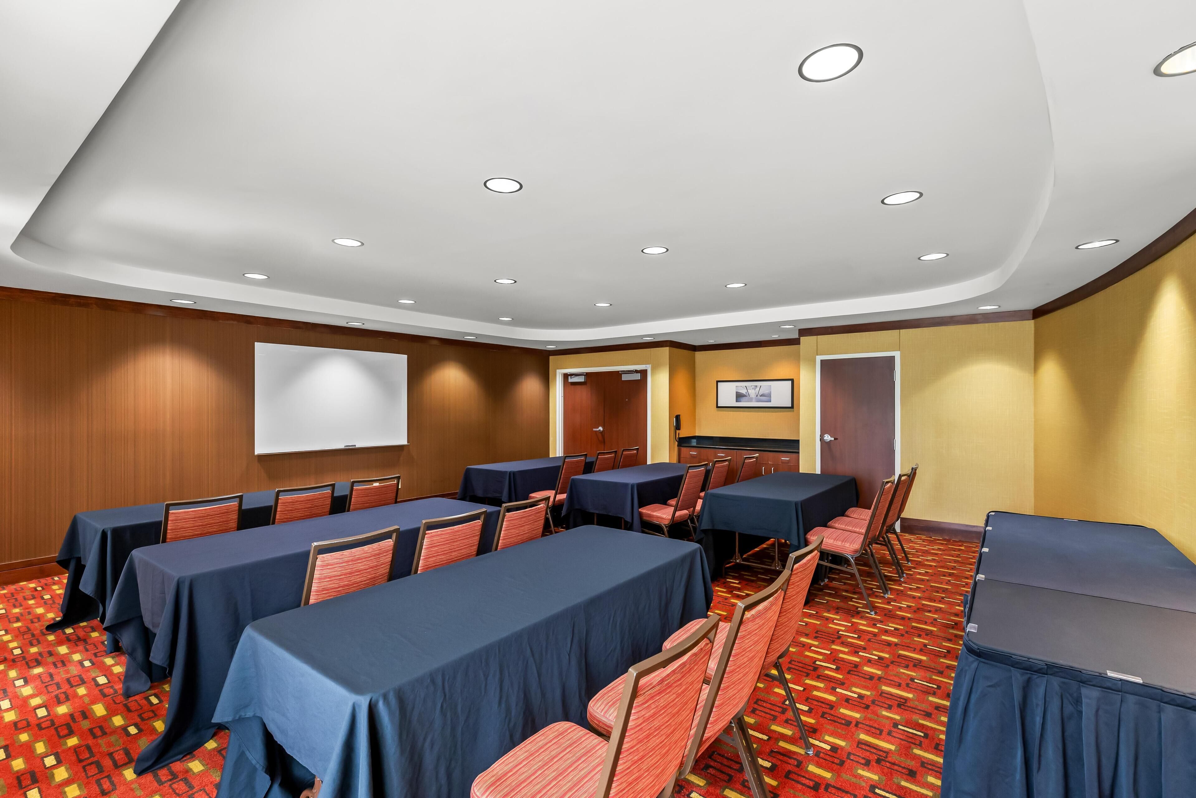 A conference room with tables, chairs, a projector screen, and a carpeted floor.