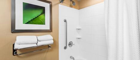 Un baño con una bañera blanca, una ducha con cabezal de ducha manual, un cuadro en la pared y un perchero con toallas dobladas.
