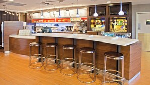 A modern bar area with a curved counter, stainless steel stools, and a menu display. - Courtyard by Marriott Louisville Northeast (Louisville)