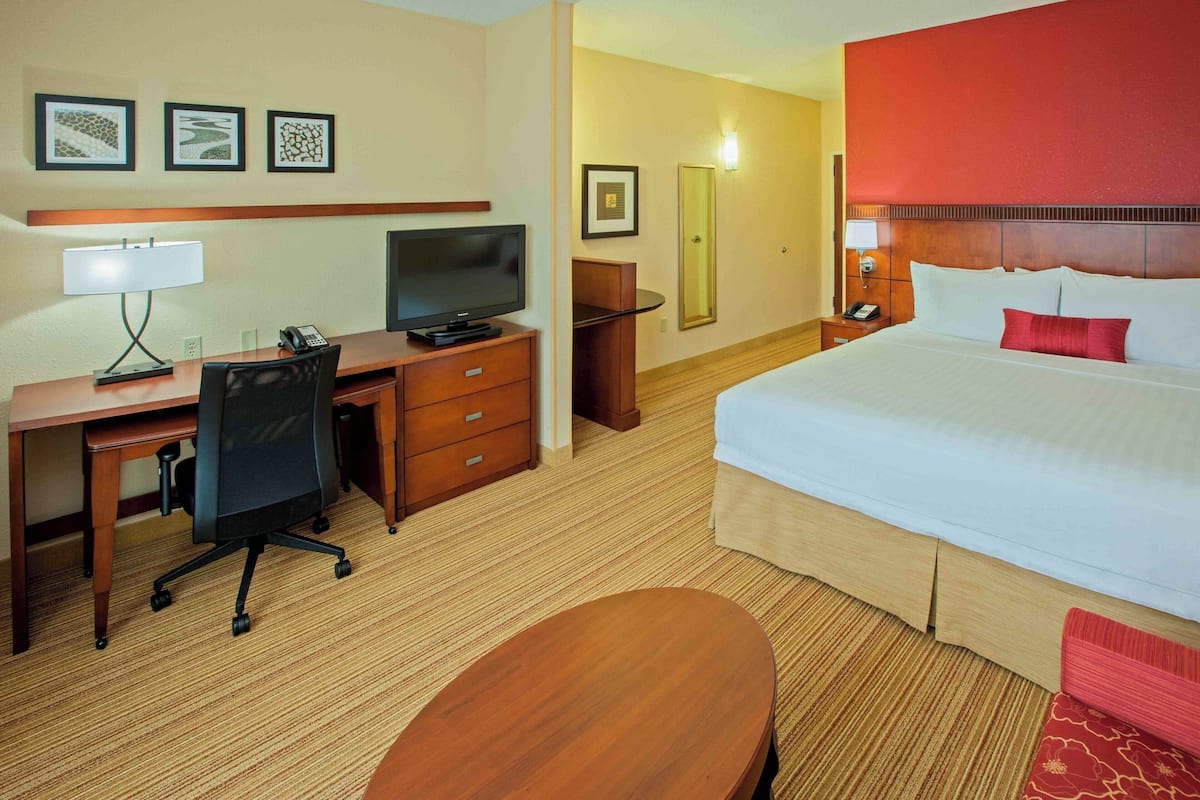 Habitación de hotel con cama, escritorio, silla, televisor y una mesita.