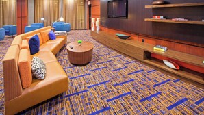 A modern hotel lobby with a sofa, chairs, a coffee table, a TV, and a patterned carpet. - Courtyard by Marriott Louisville Northeast (Louisville)