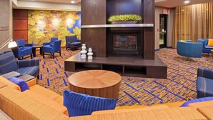 A lobby with a fireplace, seating areas, and a patterned carpet. - Courtyard by Marriott Louisville Northeast (Louisville)