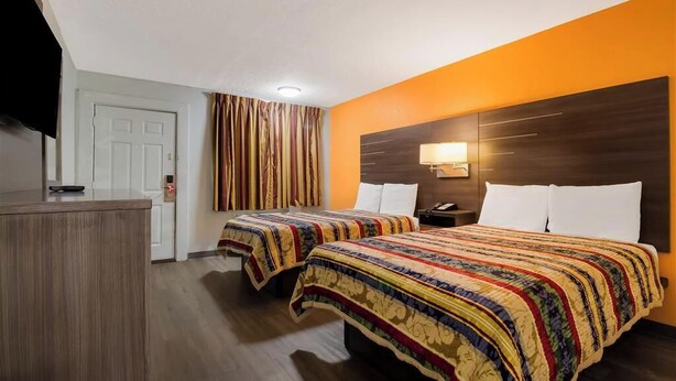 Habitación de hotel con dos camas, televisión, escritorio y puerta.