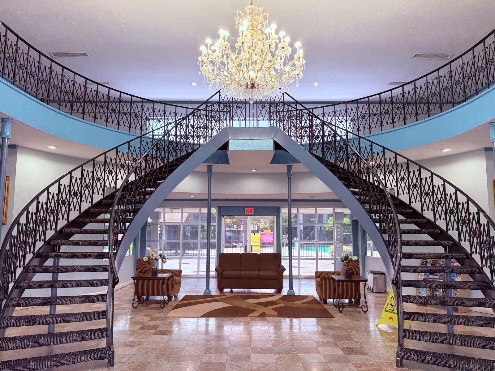 A grand staircase with a chandelier, leading to a lobby area with a sofa and a table.