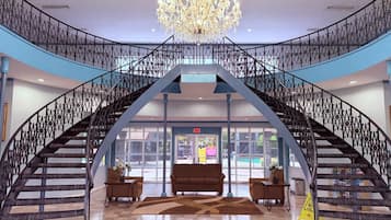 A grand staircase with a chandelier, leading to a lobby area with a sofa and a table.