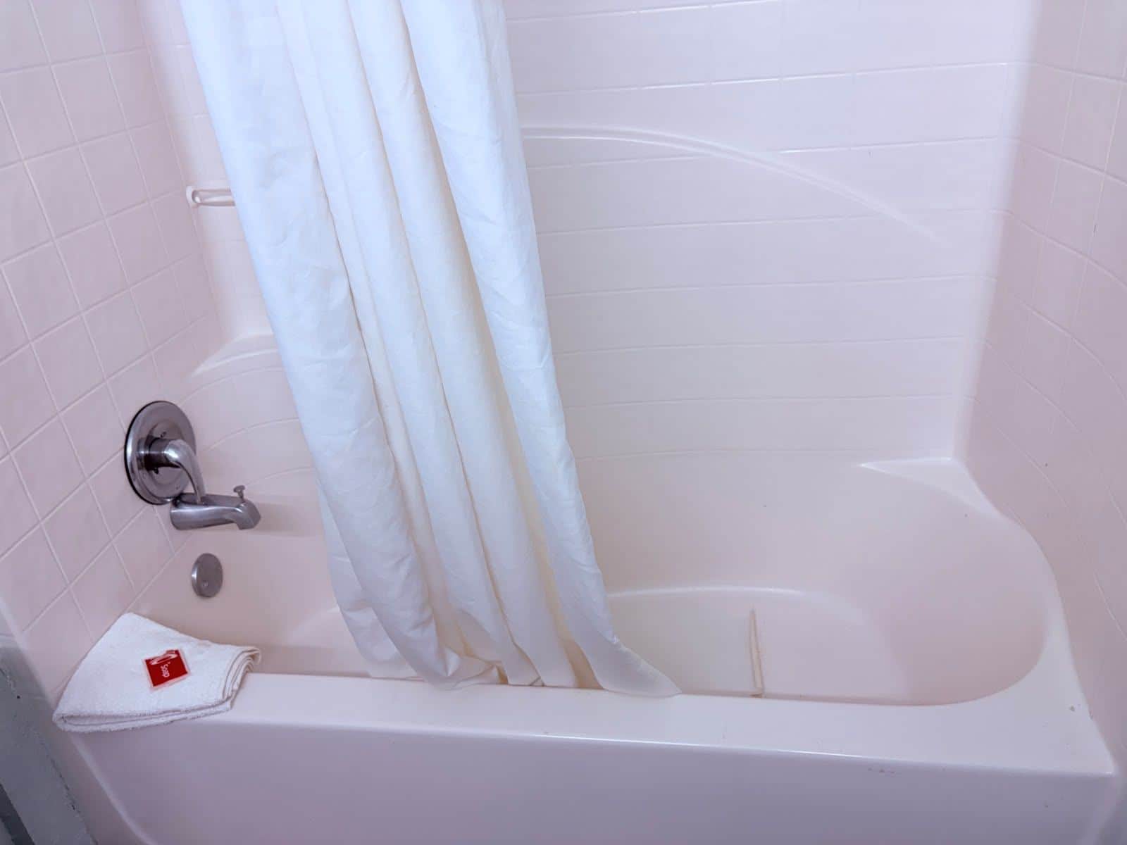 A white bathtub with a shower curtain, a towel, and a faucet.