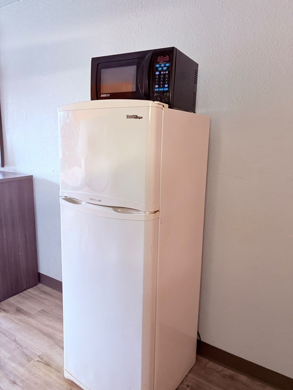 A white refrigerator with a microwave on top, a TWISTair drawer, and a wooden cabinet to the left.