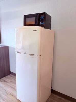 A white refrigerator with a microwave on top, a TWISTair drawer, and a wooden cabinet to the left.
