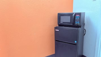 A black refrigerator with a microwave on top, positioned against a wall with an orange and blue color scheme.