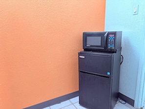 Un refrigerador negro con un microondas encima, ubicado frente a una pared con una decoración azul y naranja.