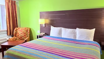 A hotel room with a bed, a chair, a nightstand, a lamp, and a window with curtains.