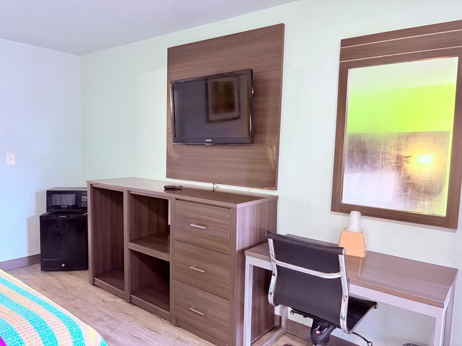 A hotel room with a bed, a desk with a chair, a television, a microwave, and a large window with a view.
