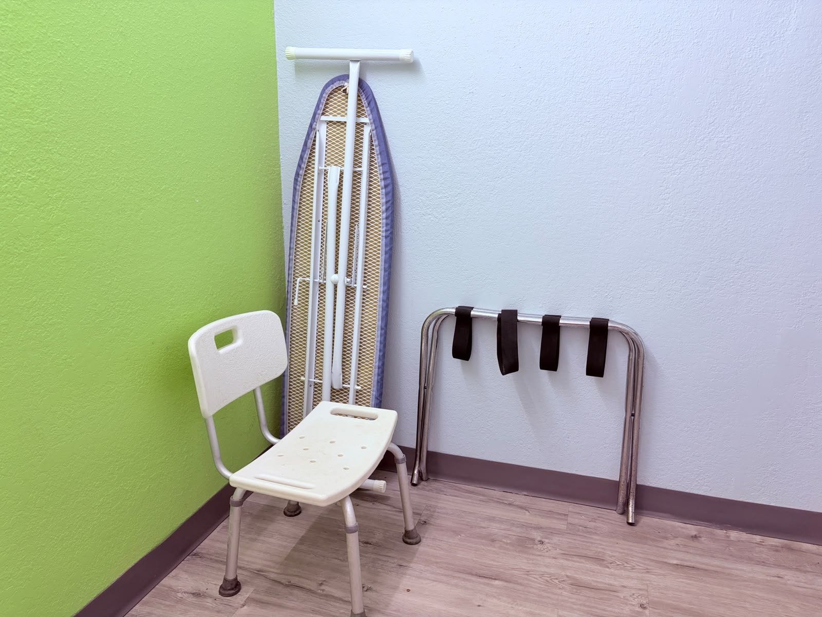 Una habitación con una pared verde, una silla blanca, una tabla de planchar y un tendedero de metal.
