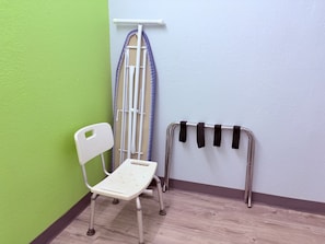 A room with a green wall, a white chair, an ironing board, and a metal drying rack.