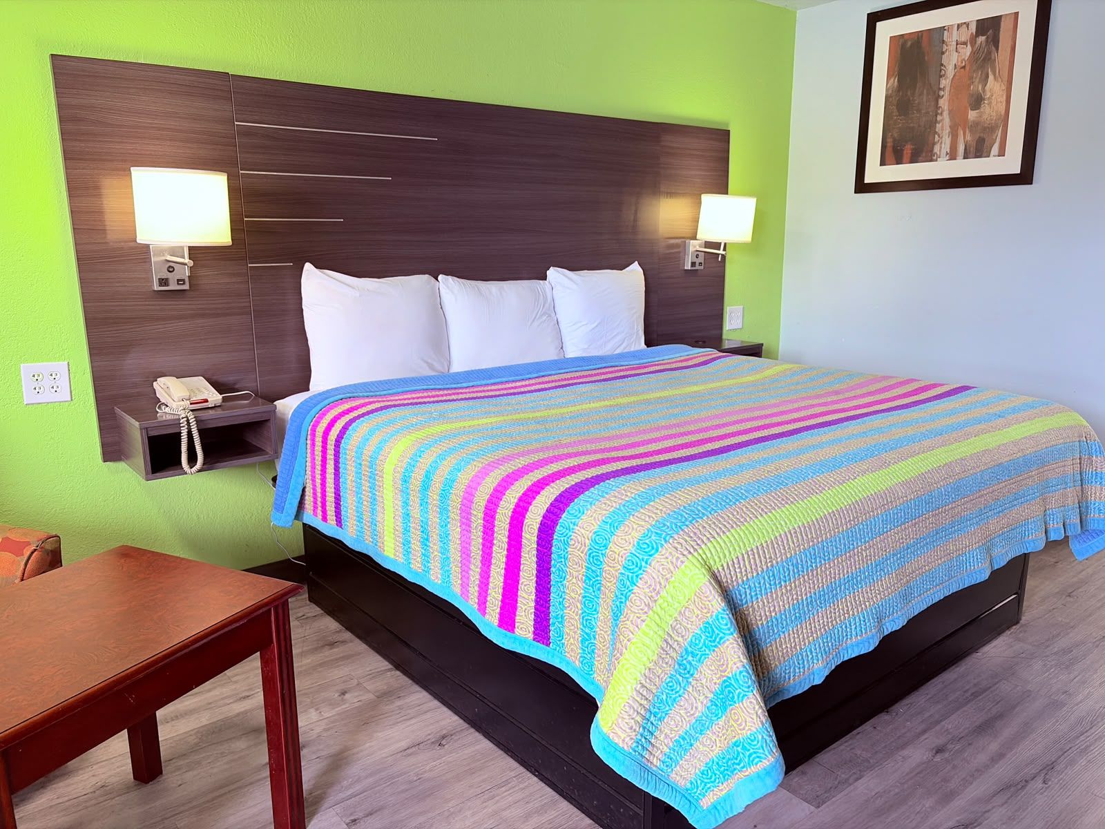 A hotel room with a bed, bedside lamps, a telephone, and a framed picture on the wall.