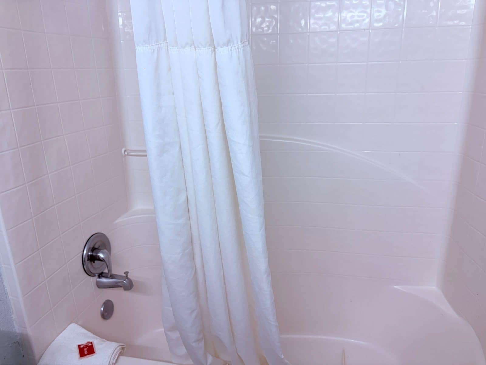 A bathroom with a white bathtub, a shower curtain, and a towel rack.