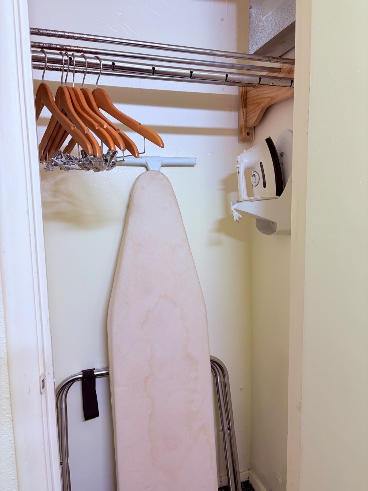 Un placard avec des cintres en bois, une planche à repasser blanche et un appareil électroménager blanc.