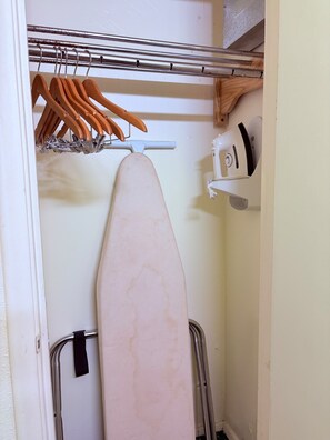 A closet with hanging wooden hangers, a white ironing board, and a white appliance. - Midtown Inn Beaumont TX near I-10 (Beaumont)