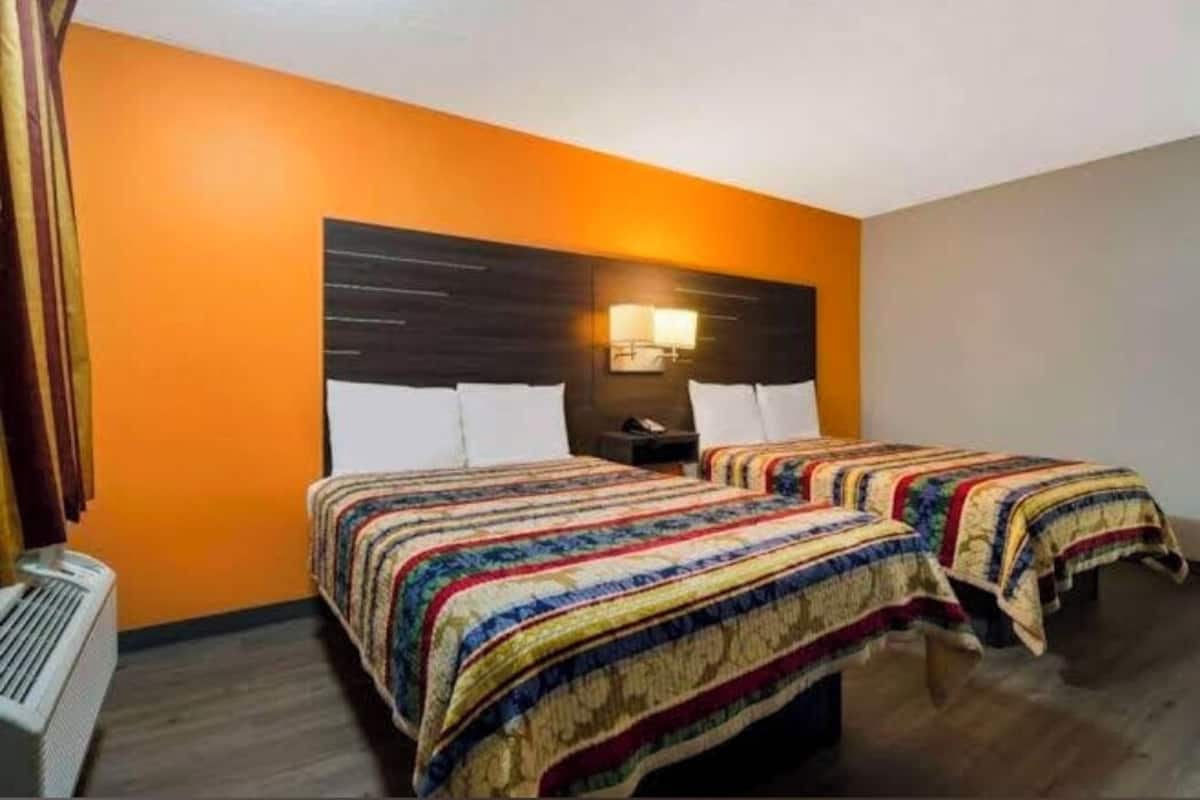 Habitación de hotel con dos camas, cabecera de madera, mesita de noche y lámpara fijada a la pared.