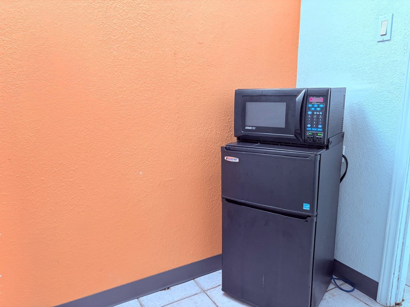 A black refrigerator with a microwave on top, positioned against a wall with a two-tone color scheme.