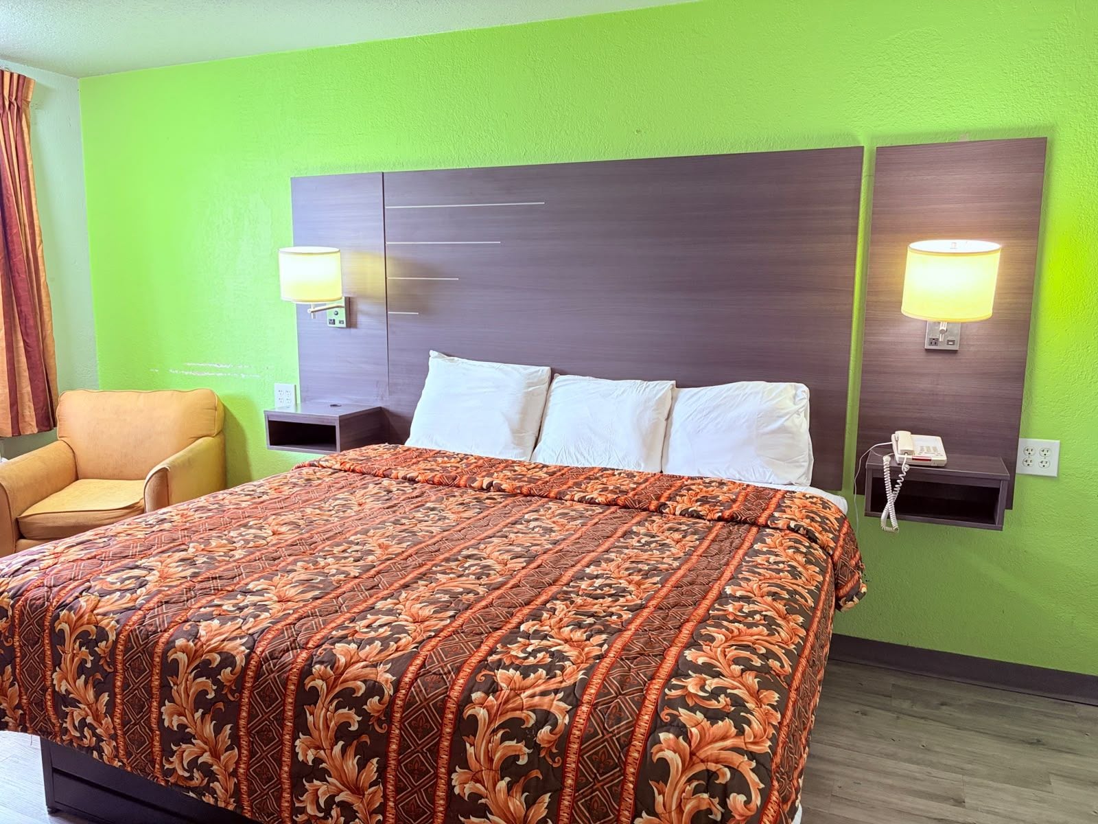 A hotel room with a large bed, two bedside lamps, a chair, and a wall-mounted telephone.