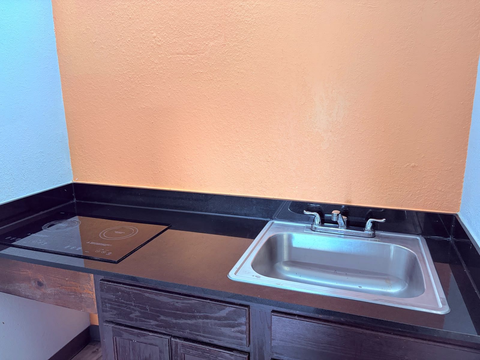 A kitchen with a black countertop, a stainless steel sink, and a built-in induction cooktop.