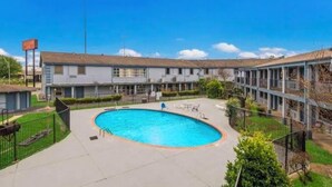 Piscina rodeada por una zona vallada, con un edificio al fondo.